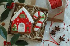 a gingerbread house decorated with icing in a box next to spools of twine