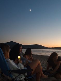 four women sitting on the beach at night drinking wine and watching the sun go down