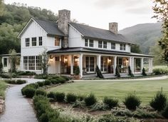 a large white house sitting on top of a lush green field next to a forest