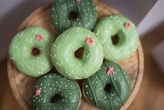 green donuts with pink flowers on them sitting in a wooden bowl