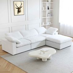 a living room with white furniture and a deer head on the wall above it's bookshelf