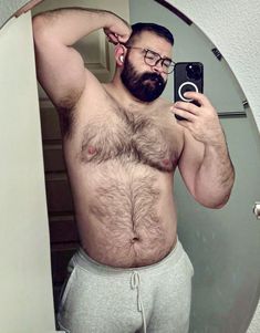 a shirtless man taking a selfie in front of a mirror with his cell phone