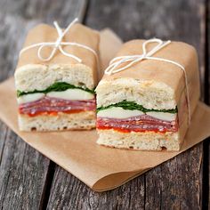 two sandwiches wrapped in brown paper sitting on top of a wooden table