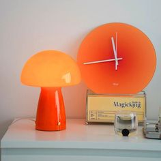 an orange lamp sitting on top of a white table next to a clock and radio