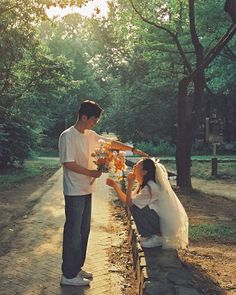 a man kneeling down next to a woman on a bench in front of some trees