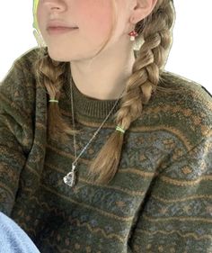 a young woman with braids wearing a green hat and sweater sitting in front of a white wall