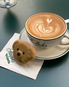 a cappuccino with a teddy bear face on it next to a cup of coffee