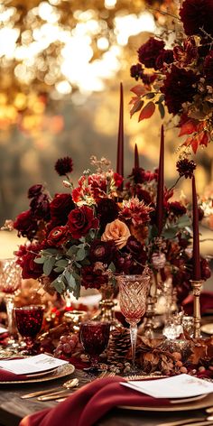 the table is set with candles, plates and red flowers in vases on it