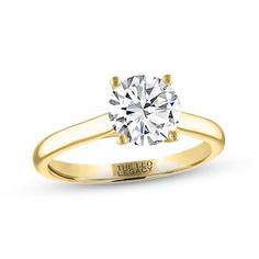 a yellow gold engagement ring with a round diamond in the center and an inscription on the side