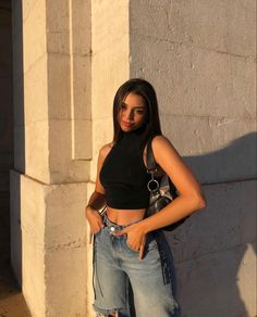 a woman standing in front of a white wall wearing ripped jeans and a black crop top