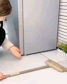 a woman kneeling down on the floor with a broom in front of her and a refrigerator behind her