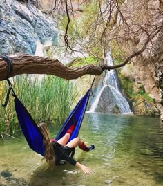 a woman laying on a hammock in the water with a waterfall behind her