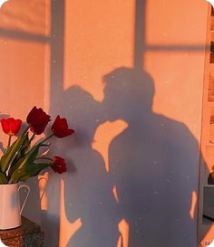 the shadow of a person standing next to a vase with flowers in it and a man's shadow