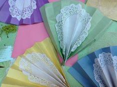 several different colored paper fans with lace doily on them sitting on a green tablecloth