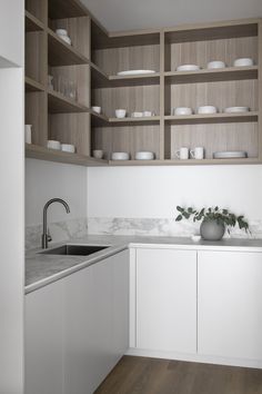 a white kitchen with wooden shelves and marble counter tops, along with an open sink