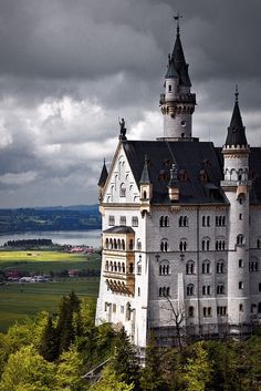 an old castle sits on top of a hill with trees in the foreground and dark clouds overhead