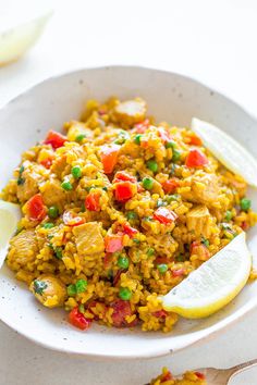 a white bowl filled with rice and peas next to lemon wedges on a table