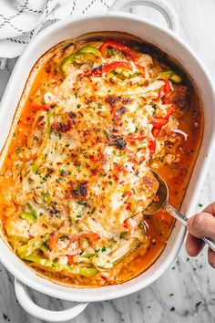 a person holding a spoon in a casserole dish with cheese and vegetables on top