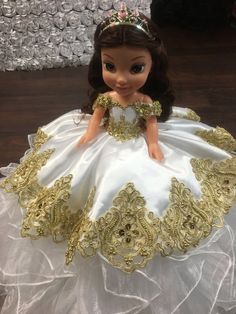 the doll is wearing a white dress with gold trimmings and a tiara