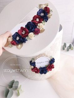 a white cake with red and blue flowers on it's top is being held up by a hand