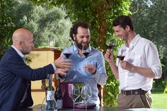 three men toasting with wine glasses in front of them on a patio table outside