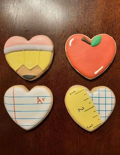 four decorated cookies on a table with ruler and apple, heart shaped cookie cutters