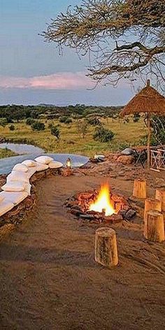 an outdoor fire pit in the middle of a field with benches and umbrellas around it