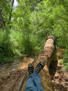 a person's feet resting on a log in the woods next to a stream