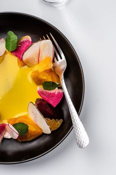 a black plate topped with sliced up fruit and a fork next to a glass of water