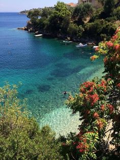 the water is crystal blue and clear with boats on it's shore, surrounded by trees