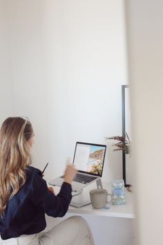 a woman sitting at a desk with a laptop and pen in her hand, writing on the screen