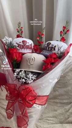 a baseball hat and flowers in a bouquet on a bed with red ribbon around it