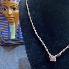 An ancient Egyptian 19.75 inch long necklace featuring tan tubular and brown disc shaped faience beads.  Hanging from the faience necklace is a brown faience amulet of Khnum (ram or ram-headed God).  Khnum was the Creator God who was thought to use a potter's wheel and primordial mud to manufacture living beings.  Circa 700 to 30 BC Creator God, Ram Head, Potters Wheel