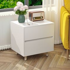 a white nightstand with a radio on it next to a yellow chair and flower vase