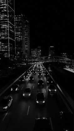 black and white photograph of cars driving down the highway at night time with skyscrapers in the background