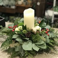 a candle is lit on top of a christmas centerpiece with greenery and berries