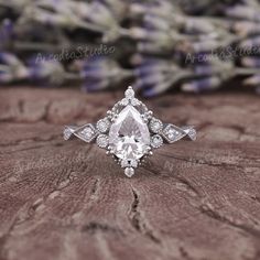 an engagement ring with a pear shaped cut diamond surrounded by small white diamonds on a piece of wood