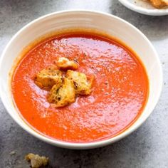 two bowls of tomato soup with bread croutons on the side and another bowl in the background