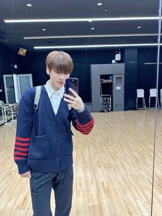 a young man standing on top of a hard wood floor holding a cell phone in his hand