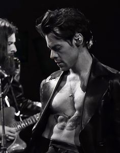 a man with no shirt on playing an electric guitar in front of a microphone and another person singing into a mic