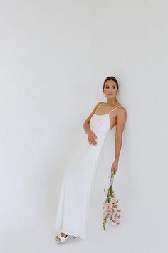 a woman in a white dress is holding flowers and posing for the camera with her hand on her hip