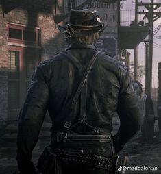 a man with a hat and leather jacket walking down a street in front of a brick building