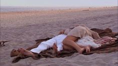 a woman laying on top of a sandy beach next to the ocean