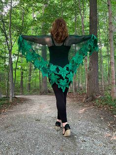 a woman walking down a dirt road in the woods wearing a green shawl and heels