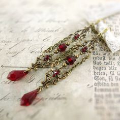 "Romantic blood red Swarovski crystals and antiqued brass filigree with an elegant Gothic design. The filigrees are connected with dangling chain and embellished with matching Swarovski crystal stones. These earrings are extra long and dangly. --------------------------------------------------------------------------------------------- Dimensions and details: - From the top of the ear wire to the bottom of the earrings, they measure approximately 3 1/4\" inches (83mm) - Beads, pearls, teardrops, Red Vintage Chandelier Dangle Earrings, Red Vintage Dangle Chandelier Earrings, Vintage Red Dangle Chandelier Earrings, Vintage Red Brass Earrings, Vintage Red Teardrop Jewelry, Ornate Red Filigree Earrings, Handmade Gothic Wedding Earrings, Formal Red Brass Earrings, Victorian Red Jewelry For Wedding