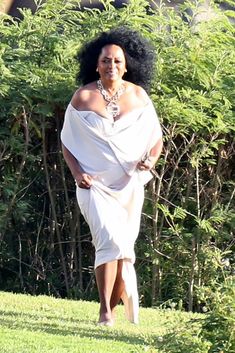 a woman in a white dress is walking through the grass