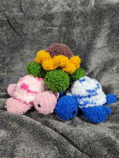 three small stuffed animals sitting on top of a gray blanket next to eachother