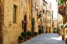 an alley way with potted plants on either side and stone buildings in the background