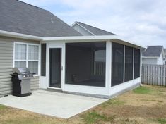 a small gray house with a screened porch and grill in the front yard, on a sunny day