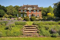 a large brick house surrounded by lush green grass and bushes with steps leading up to the front door